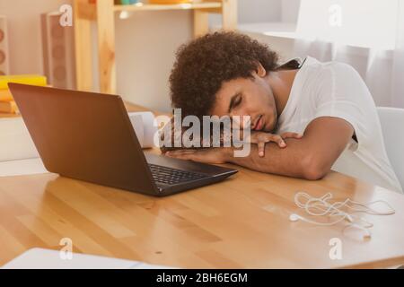 Müde Mann lehnte Ellbogen auf den Tisch und schloss die Augen, während der Arbeit am Computer. Auf dem Schreibtisch befindet sich ein Laptop und andere Werkzeuge für die Büroarbeit Stockfoto
