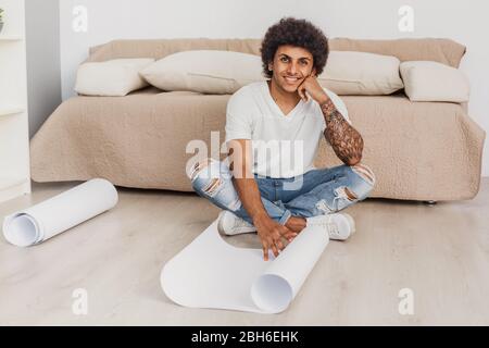 Positiv Lockenhaarige Mann öffnet ein leeres Blatt Papier für Zeichnungen, sitzen auf dem Boden zu Hause Stockfoto