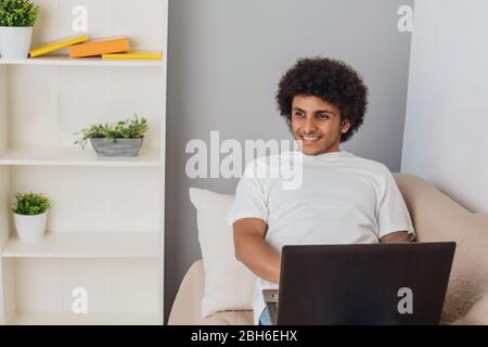 Entspannen Sie sich zu Hause auf der Couch. Attraktiver Mann arabische Nationalität ruht, Laptop auf die Beine und lächelt. Stockfoto