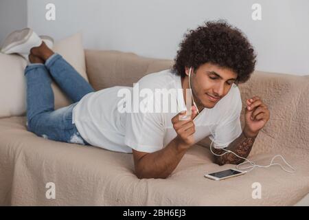 Lockig behaart stilvolle Mann Augen geschlossen liegen auf der Couch zu Hause, genießen Sie die Musik. Stockfoto