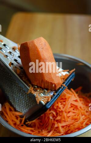 Ein großes Stück Karotten liegt auf einer Reibe. Unterbrochener Zerkleinerungsprozess rohes Gemüse. Der Prozess der Herstellung von Salat. Im echten Leben. Nahaufnahme. Selektiv fo Stockfoto
