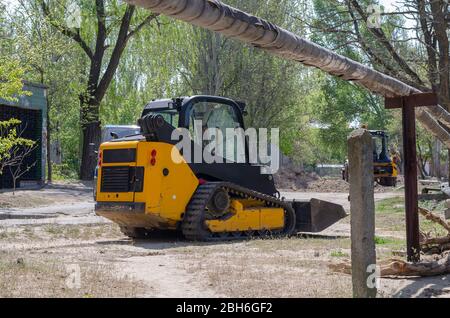 Kleiner Raupenbagger mit Gummigleisen. Gelber Kompaktlader an einer Straße in der Stadt, die mit Erde arbeitet. Industriemaschinen. Branche. Stockfoto