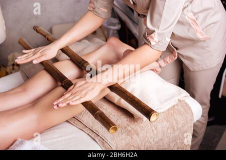 Massage des menschlichen Fußes im Spa-Salon mit Bambusstäbchen. Beinabschluss, kaukasische Frau mit einem Massage-Spa-Salon Stockfoto