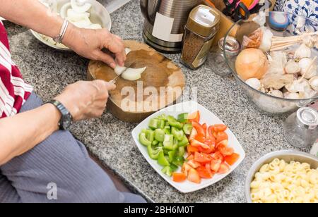 Draufsicht auf ältere Frau Hände hacken Zwiebel auf Holzbrett in der Küche. Stockfoto