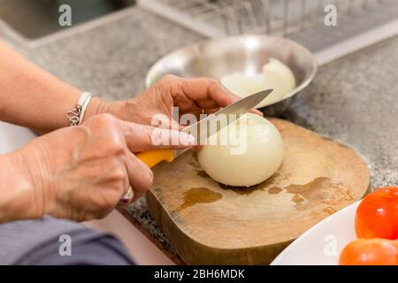 Ältere Frau Hände hacken Zwiebel auf einem Holzbrett in der Küche. Stockfoto