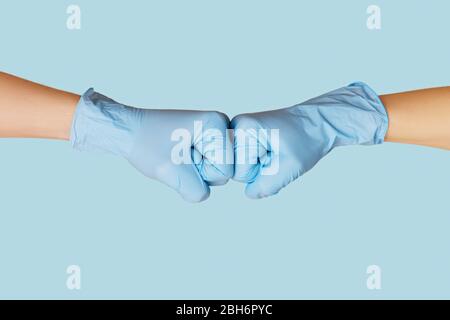 Hände in medizinischen Handschuhen begrüßen sich mit Faust Bump auf blauem Hintergrund. Stockfoto