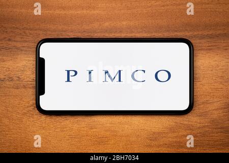 Ein Smartphone mit dem PIMCO Logo liegt auf einem einfachen Holztisch (nur redaktionelle Verwendung). Stockfoto