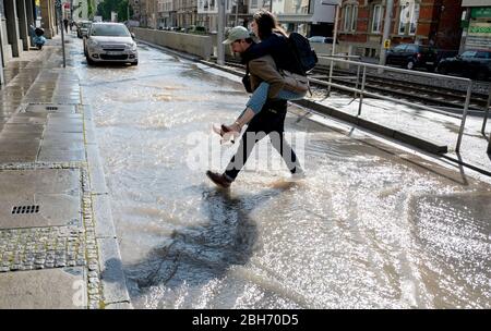 Stuttgart, Deutschland. April 2020. Ein Mann trägt eine Frau auf seinen Schultern über eine Straße, die von einem gebrochenen Wasserrohr überflutet wird. Quelle: Marijan Murat/dpa/Alamy Live News Stockfoto