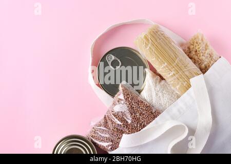 Textil Lebensmitteltasche mit Lebensmitteln Krise Lebensmittelvorrat für Quarantäne Isolationsperiode auf rosa Hintergrund. Reis, Buchweizen, Nudeln, Dosenfutter. Essen Stockfoto