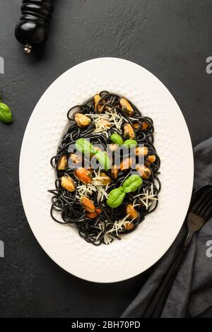 Schwarze Pasta Spaghetti Tintenfisch Tinte mit Muscheln in weißem Teller auf schwarzem Hintergrund. Draufsicht. Kopierbereich. Stockfoto