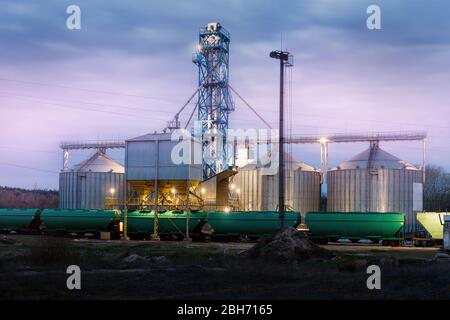 Moderne Stahl landwirtschaftlichen Getreidespeicher Silos Getreidespeicher Lager Verladung Eisenbahn Fracht Wagen bei Nacht oder Sonnenaufgang. Agribuisness Ackerland ländlichen Stockfoto