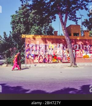 Pakistan, Islamabad Straßenszene mit ein paar Damen in sehr bunten Kleidern, die ein Plakatschild mit Porträts berühmter pakistanischer Filmstars passieren Stockfoto