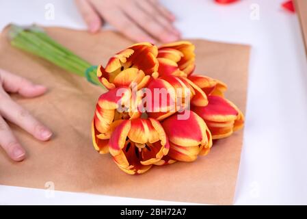 Junge weibliche Floristin ist eine rote Farbe Tulpe Blumenstrauß für Muttertag Geschenk mit Krawatte Band Schleife über einem weißen Tisch Hintergrund, Nahaufnahme, l wickeln Stockfoto