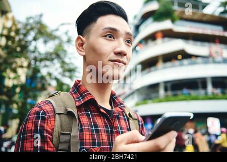 Asian Mann hält Handy und schaut weg Stockfoto