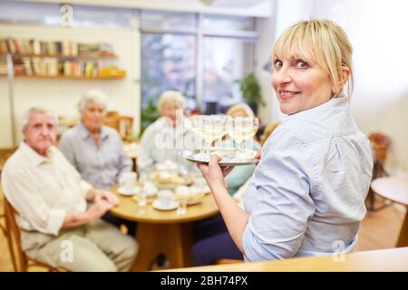 Kellnerin serviert Weißwein für eine Gruppe von Senioren bei der Seniorenversammlung Stockfoto