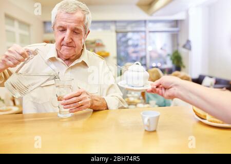 Senior gießt Wasser aus einer Karaffe in ein Glas im Gemeinschaftsraum des Seniorenheims Stockfoto