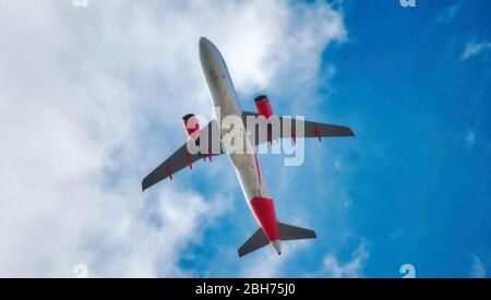 Unterbauch eines in der Luft fliegenden Düsenflugzeugs isoliert gegen einen blauen Himmel mit Wolken Stockfoto