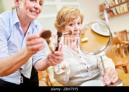 Alte Frau im Make-up Kurs, die zusammen mit einem Make-up Künstler vor dem Spiegel stylen Stockfoto