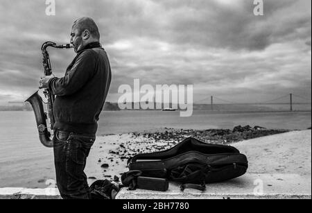 Lissabon, Portugal - 10. Februar 2020: SAX-Straßenmusiker in der Nähe von Praza do Comercio, Lissabon, Portugal. 25 de Abril Brücke unten Stockfoto