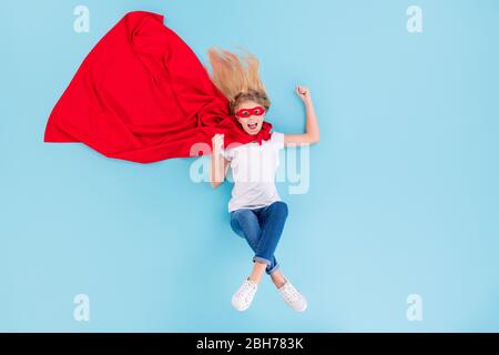 Top über hohen Winkel Ansicht in voller Länge Foto von verrückt begeistert Kind kleine Superfrau speichern Welt heben Fäuste schreien ja tragen rote Cape Maske weißen Denim Stockfoto