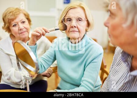Ältere Frau mit dem Make-up Pinsel beim Make-up Styling im Schminkkurs im Altersheim Stockfoto