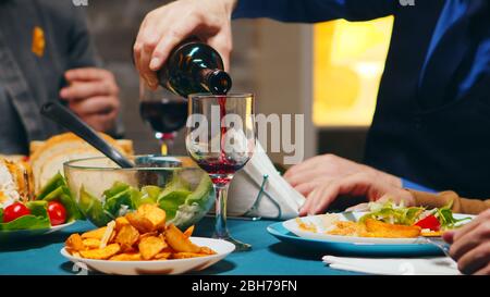 Zoom in Bild eines jungen Mannes, der Rotwein in ein Glas beim Familienessen eingießt. Stockfoto