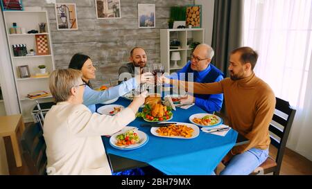 Von oben gesehen, wie die Familie mit Rotwein anklirrt, während sie beim Abendessen mit köstlichen Speisen anstoßen. Stockfoto