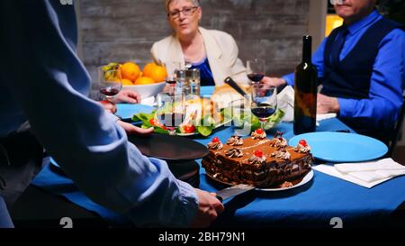 Folgen Sie der Aufnahme einer jungen Frau, die ihrer Mutter beim Familienessen ein Stück Kuchen gibt. Stockfoto
