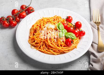 Pasta mit Tomatensauce und Kirschtomaten mit Basilikum auf weißem Hintergrund. Italienische Spaghetti werden typischerweise aus Hartweizengrieß hergestellt Stockfoto