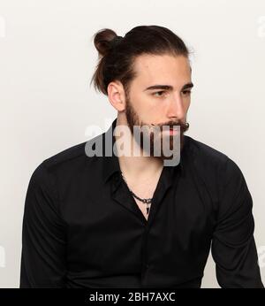 Junge, modische männliche Modell mit langen Haaren und Bart posiert im Studio auf isoliertem Hintergrund. Mode, Business, Modellierungskonzept. Stockfoto