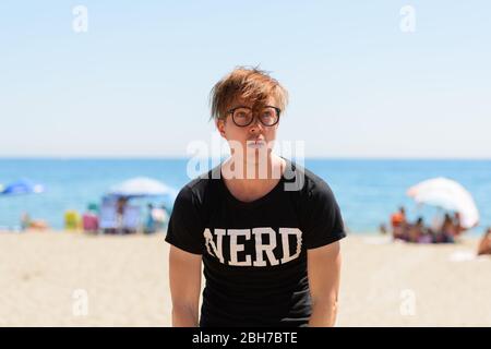 Gestresste junge Nerd Mann sieht gelangweilt und müde am Strand Stockfoto