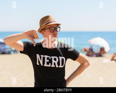 Gestresste junge Nerd-Tourist Mann gibt Daumen unten am Strand Stockfoto