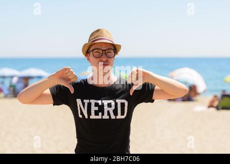 Gestresste junge Nerd-Tourist Mann gibt Daumen unten am Strand Stockfoto