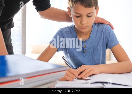 Kind sitzt am Tisch mit vielen Büchern Notizbücher und Hausaufgaben zu machen. Mutter hilft ihm. Lernschwierigkeiten, Lernen zu Hause, Bildung zu Hause Stockfoto