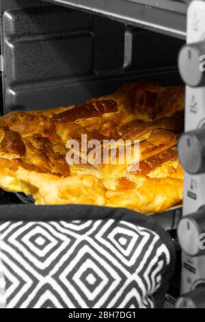 Kröte im Loch, Yorkshire Pudding mit Schweinewurst, die von einer Person mit Ofenhandschuhen aus dem Ofen genommen wird. Selektives Farbbild Stockfoto