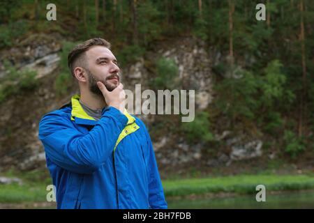 Taille oben von jungen bärtigen Mann allein im Freien mit Natur auf Hintergrund stehen. Lifestyle-Konzept für Reisen Stockfoto