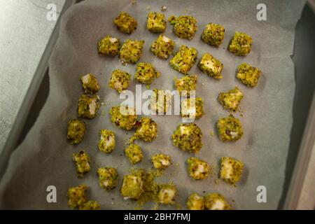 Würfel von Feta-Käse mit gemahlenen Pistazien bedeckt sitzen auf einem Backblech bereit, in den Ofen zu gehen Stockfoto