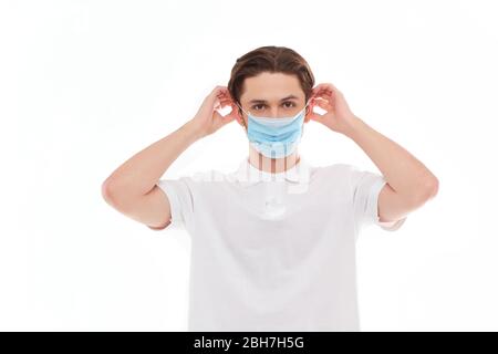 Ein Mann in einem weißen T-Shirt von europäischem Aussehen zieht eine medizinische Maske an. Isoliert auf weißem Hintergrund Stockfoto