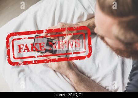 Fake News Infosemics during Covid-19 Pandemie Concept. Mann hält Handy und liest zu Hause Nachrichten oder soziale Netzwerke. Letzte News lesen upd Stockfoto