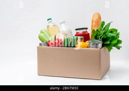 Spendenbox mit Zubehör Nahrung für Menschen in Isolation auf hellem Hintergrund. Wesentliche Güter: Öl, Konserven, Getreide, Milch, Gemüse, Obst. Stockfoto