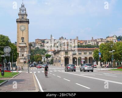 Bergamo, Italien - 06. August 2019: Radler auf den Straßen im unteren Teil der Stadt Bergamo mit Blick auf den Turm Torre dei Caduti und die befestigte obere Stockfoto