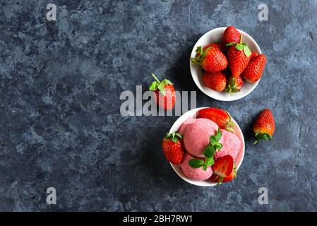 Erdbeer-Eisschaufel mit frischen Erdbeeren in der Schüssel über blauem Steingrund mit freiem Text. Leckeres kaltes Sommerdessert. Draufsicht, flach Stockfoto