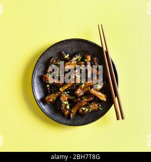 Bulgogi Aubergine auf Teller über gelbem Hintergrund braten. Gebratene Aubergine im koreanischen Stil. Draufsicht, flaches Lay Stockfoto