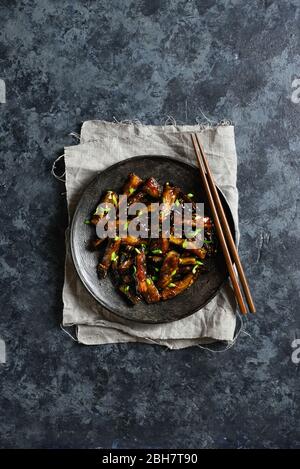 Gebratene Aubergine im koreanischen Stil. Rührbraten Bulgogi Aubergine auf Platte über dunklem Steinhintergrund mit freiem Textraum. Draufsicht, flaches Lay Stockfoto