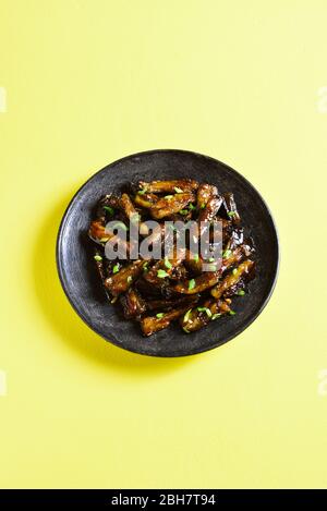 Braten Bulgogi Aubergine auf Platte über gelbem Hintergrund mit freiem Textraum. Gebratene Aubergine im koreanischen Stil. Stockfoto