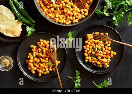 Knusprig geröstete Kichererbsen im indischen Stil auf schwarzem Steingrund. Vegetarisches veganes Food Konzept. Draufsicht, flaches Lay Stockfoto