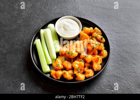 Nahaufnahme von Blumenkohl Büffelflügeln mit Sellerie und Sauce auf Platte auf schwarzem Steingrund. Gesunde Ernährung, pflanzliche Lebensmittel Konzept. Stockfoto