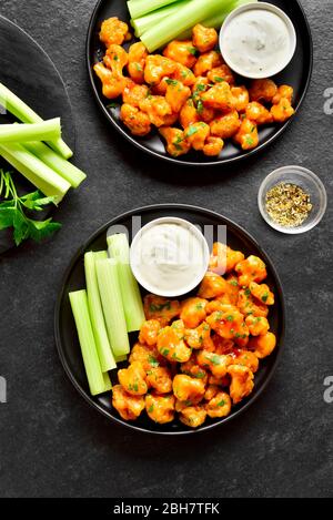 Blumenkohl Büffelflügel mit Sellerie und Sauce auf Platten auf schwarzem Steingrund. Gesunde Ernährung, pflanzliche Lebensmittel Konzept. Draufsicht, flaches Lay Stockfoto