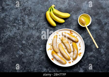 Frittierte Bananen auf weißem Teller über blauem Steinhintergrund mit freiem Textbereich. Leckeres Dessert aus panfrittierten Bananen im asiatischen Stil. Draufsicht, flach Stockfoto