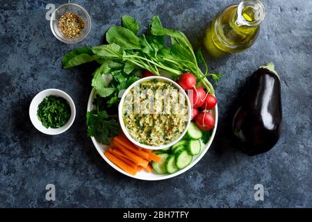 Baba ganoush (geröstete Auberginen-Dip) in Schüssel und frisches Bio-Gemüse auf blauem Steingrund. Gesunde Ernährung. Vegetarisches veganes Food Konzept. Bis Stockfoto